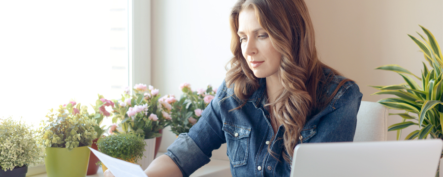 A woman in front of a laptop looking at a paper